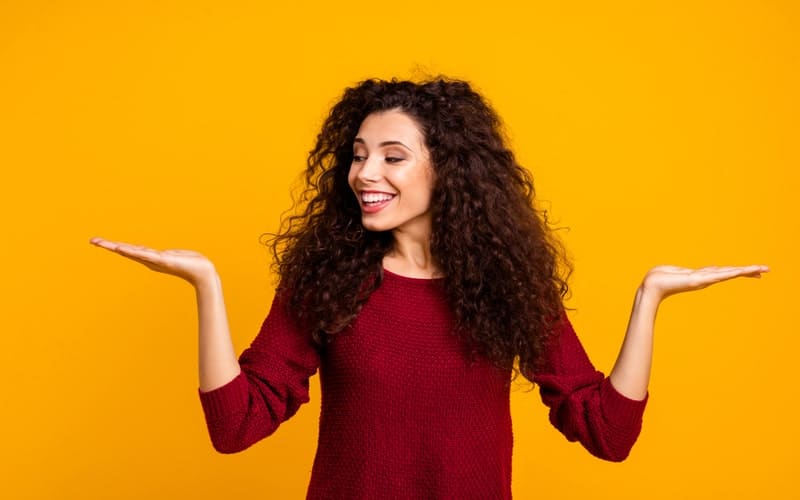  Une femme portant un pull-over bordeaux lève les mains, paumes tournées vers le haut.