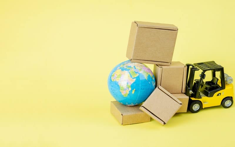 A toy yellow forklift carrying a small globe and five small boxes with a yellow background