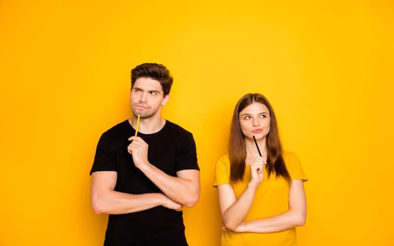 Un homme portant un t-shirt noir et tenant un crayon jaune et une femme portant un t-shirt jaune doré et tenant un crayon noir réfléchissent ensemble