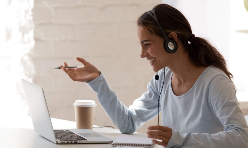 A woman wearing headphones while talking to a customer in front of her laptop.