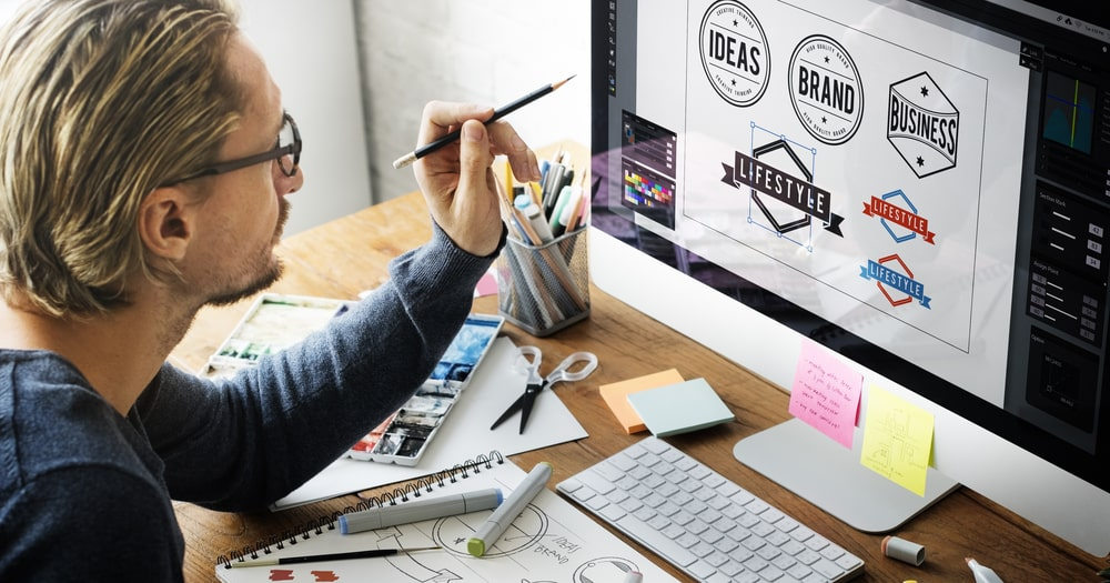 une personne assise à un bureau, regardant un écran d'ordinateur et créant des logos de marque