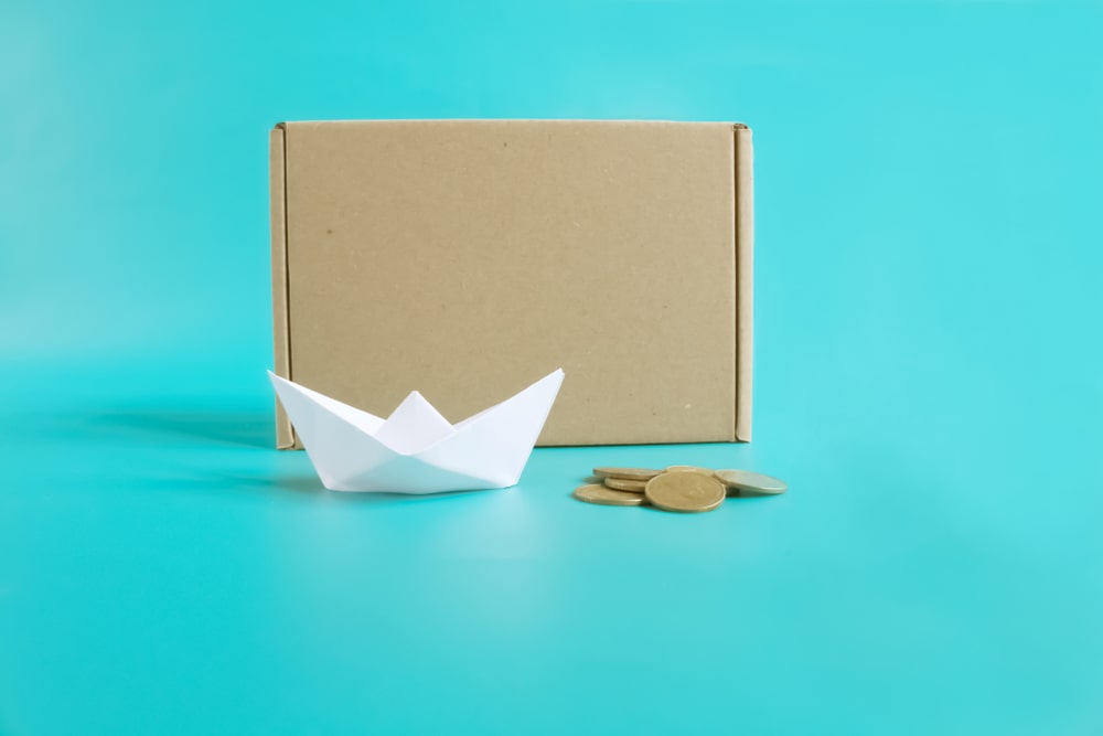 un bateau en papier et des pièces de monnaie à côté d'une boîte d'expédition