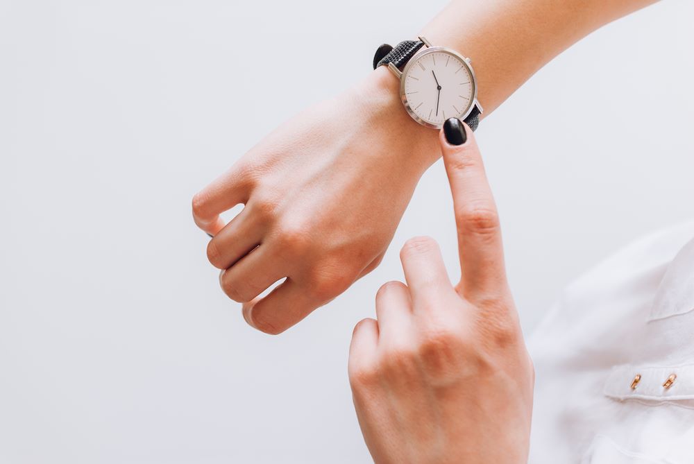 A hand pointing at a watch on a wrist