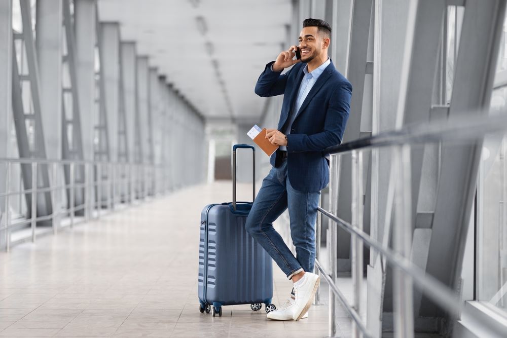 A smiling man with a suitcase using his phone in airport