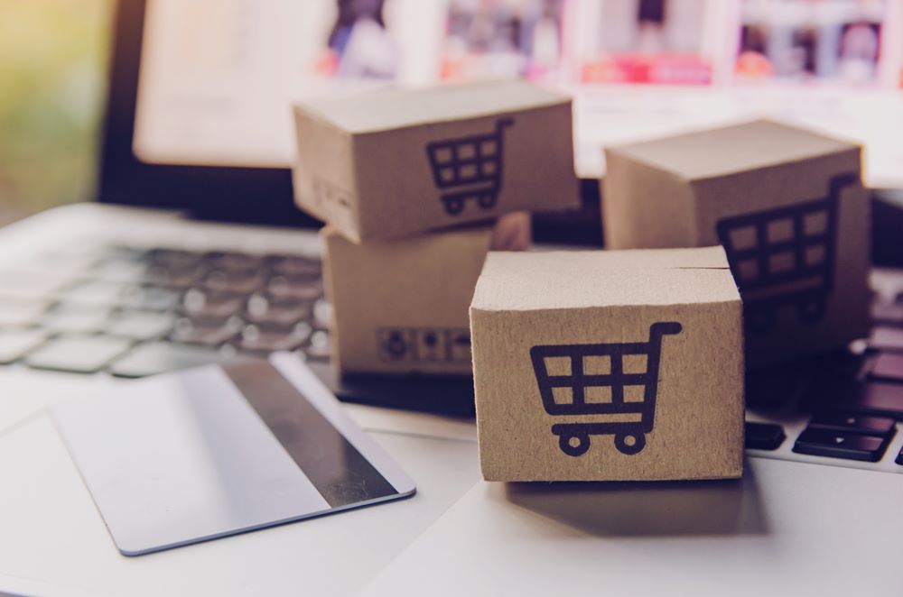 Miniature boxes with shopping cart icons and a card on top of a laptop