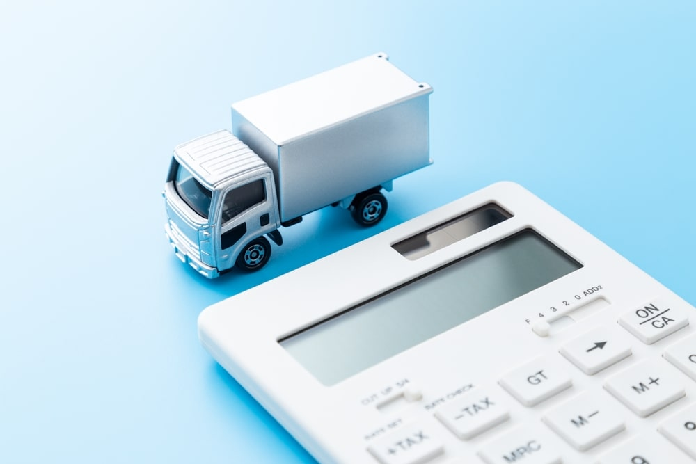 A small toy delivery truck next to a white calculator on a blue background.