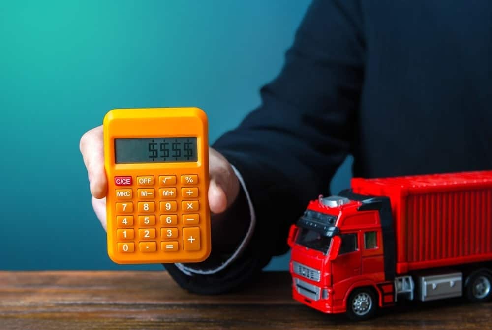 A hand holding a small yellow calculator with a red truck on the side