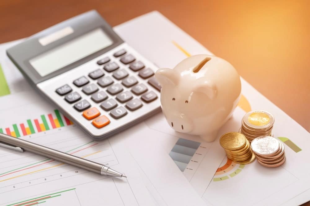 A piggy bank with a calculator on top documents with coins on the side