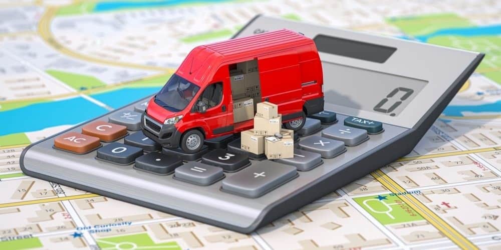 A red delivery van toy with small stack of boxes on top of a calculator and map