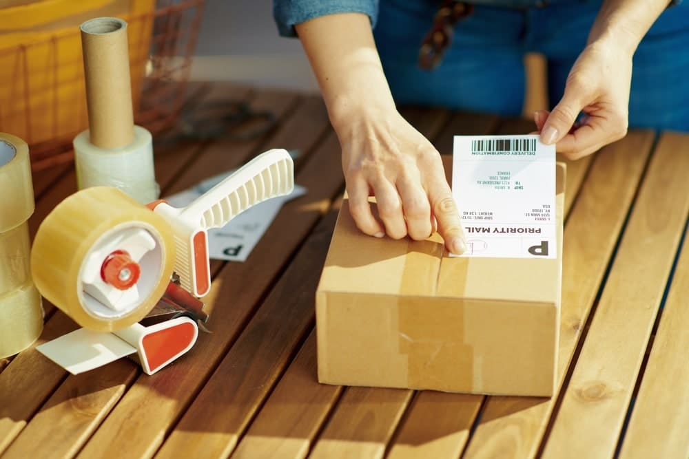 bunch of tapes and a person attaching priority mail sticker on box